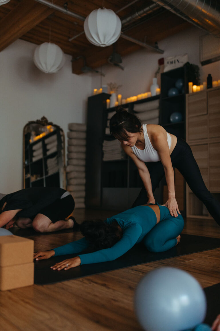 OHA Wellness instructor providing hands-on adjustments to a student during a yoga session in Liberty Village, Toronto.